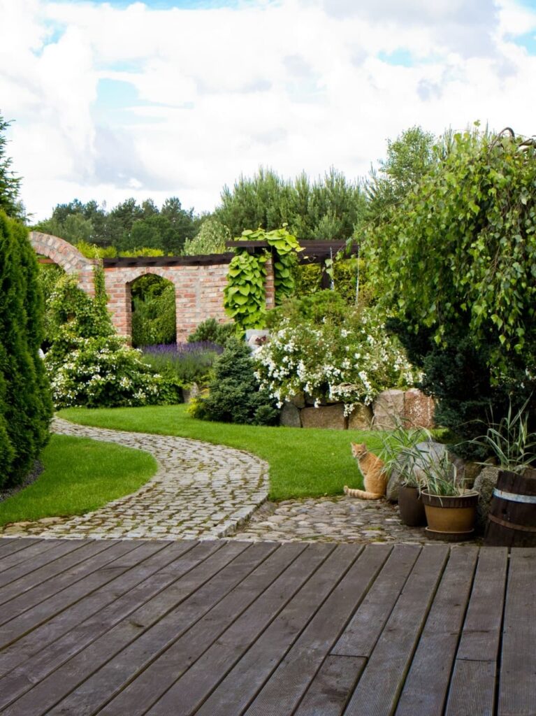 Liebevoll angelegter Garten mit geschwungenem Natursteinweg, üppigen Sträuchern und blühenden Pflanzen als grüne Erweiterung des Wohnraums.